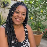 Mulher de tranças sorrindo ao lado de uma frutífera plantada em vaso no quintal